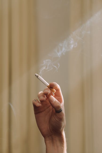 Close-up view of two discarded cigarette butts on a tiled outdoor surface with small pebble insets, with one butt in focus showing ash and burnt cigarette filter, while the other is slightly blurred i